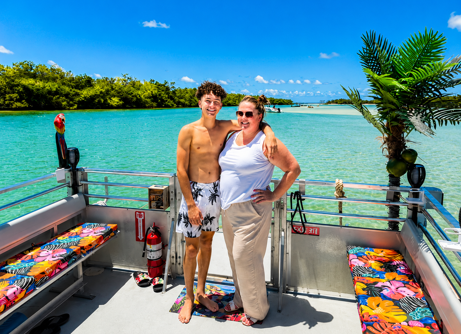 Two guests posing on the tiki boat with turquoise water behind them
